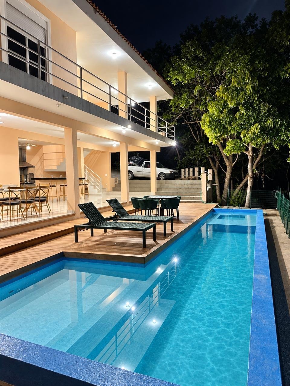 Rancho iluminado à noite com piscina, deck de madeira e jardim paisagístico
